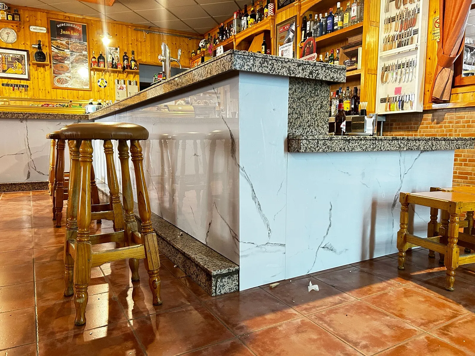 Barra de bar con revestimiento Kobert In efecto mármol y taburetes de madera