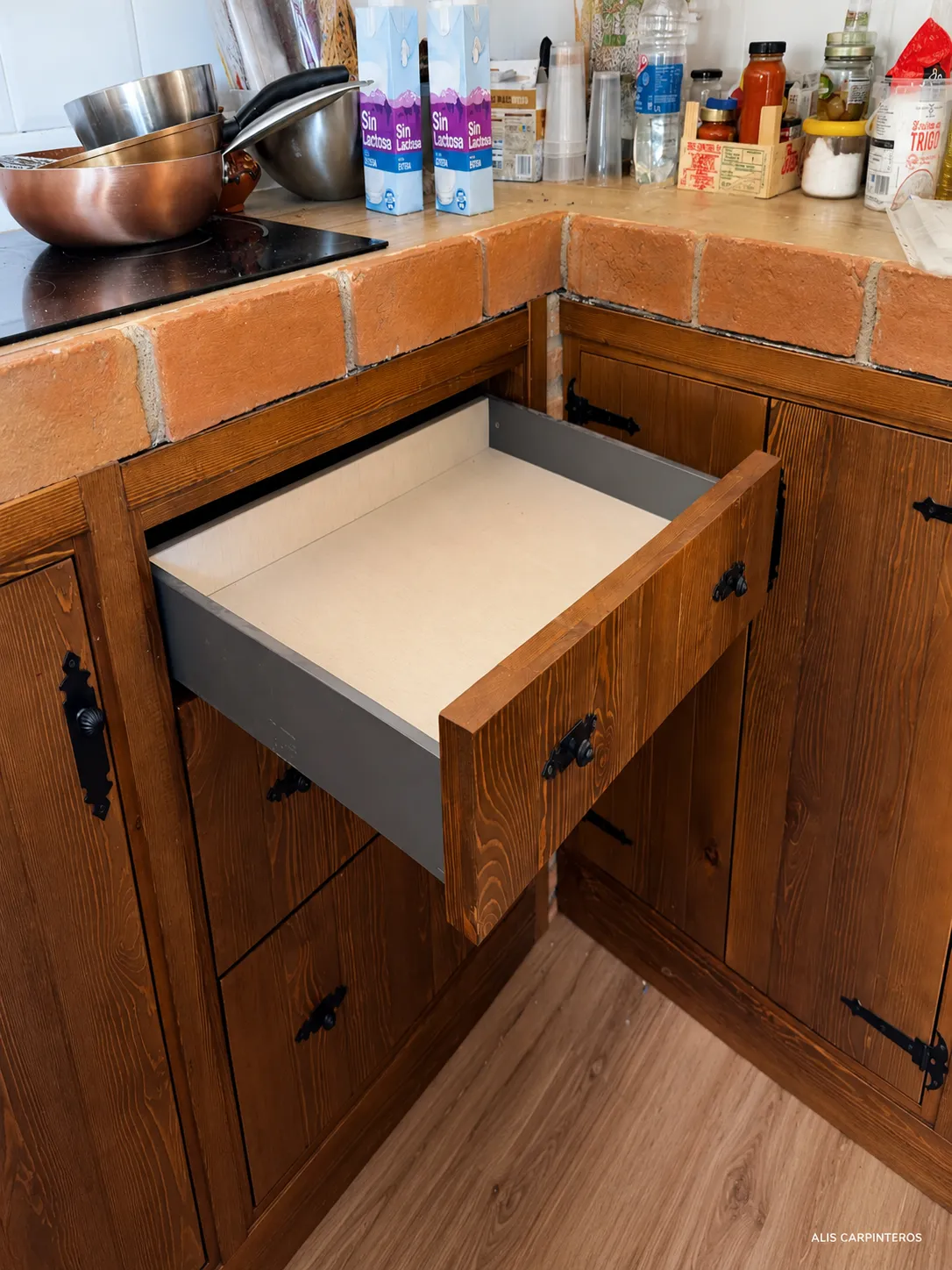 Cajón abierto de la cocina rústica con guías metálicas y frente de madera